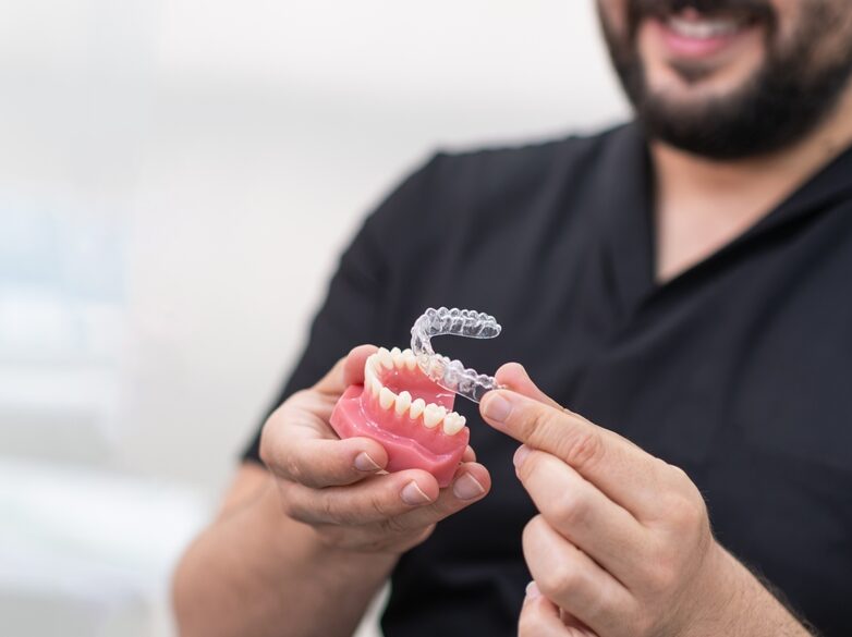 Cheerful Dentist Putting Transparent Aligners On Artificial Lower Jaw